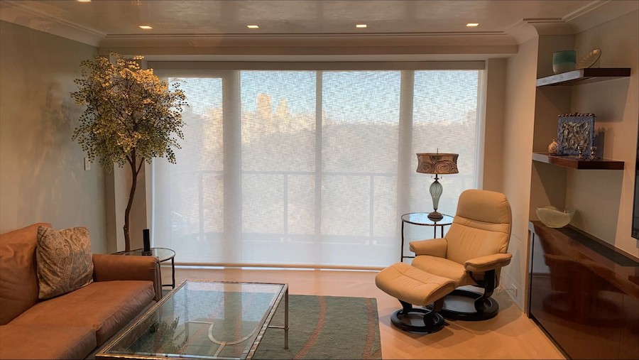 large living room windows covered with sheer motorized shades with light filtering through