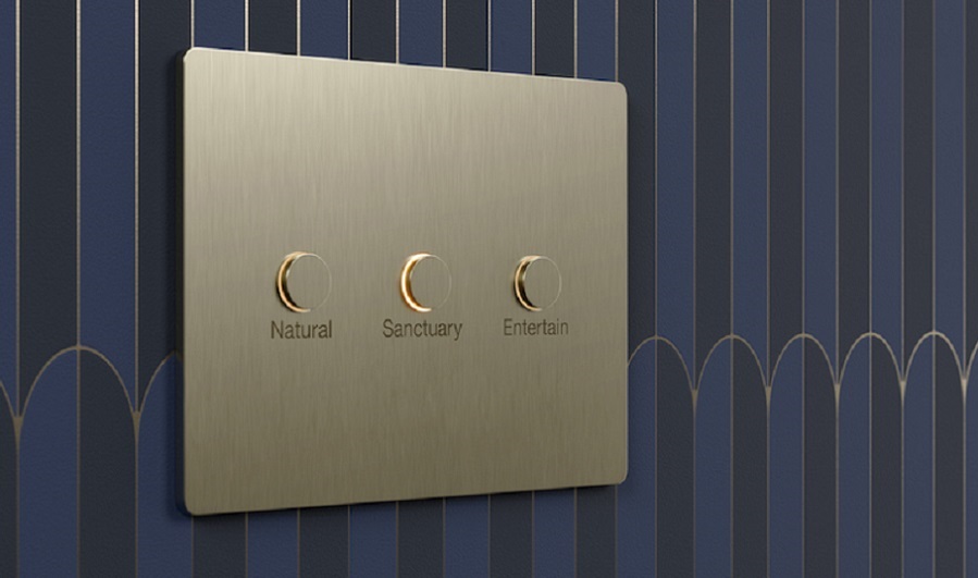 Gold Lutron Alisse keypad mounted on a blue and black wallpapered wall. Three buttons read natural, sanctuary, and entertain.  